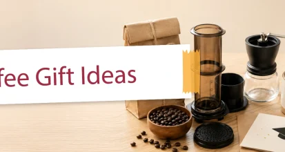 An assortment of coffee gift items including an AeroPress, beans, and a ceramic mug arranged for a graduation gift