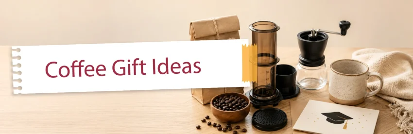 An assortment of coffee gift items including an AeroPress, beans, and a ceramic mug arranged for a graduation gift