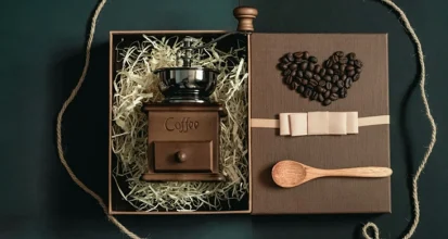 Coffee gift box with a vintage wooden hand grinder in shredded paper, a heart made of roasted coffee beans on the lid, and a wooden scoop
