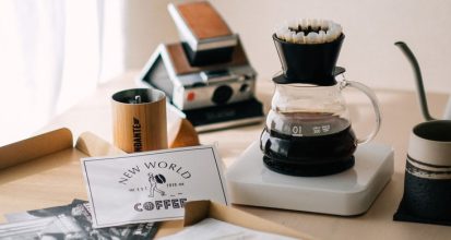 Pour-over dripper, kettle, mug, and hand grinder arranged as coffee gift ideas with wrapped kraft paper