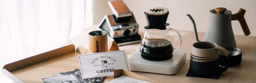 Pour-over dripper, kettle, mug, and hand grinder arranged as coffee gift ideas with wrapped kraft paper