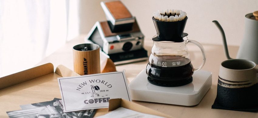 Pour-over dripper, kettle, mug, and hand grinder arranged as coffee gift ideas with wrapped kraft paper