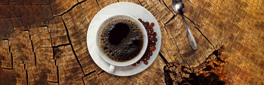 Overhead view of a cup of black coffee on a rustic wooden surface with scattered coffee beans and a spoon