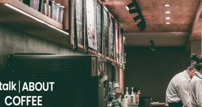 Interior of a coffee shop with two baristas working behind the counter in a dark, industrial-style cafe
