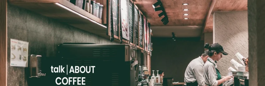 Interior of a coffee shop with two baristas working behind the counter in a dark, industrial-style cafe
