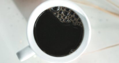 Cup of black coffee on a wooden surface next to a small notebook, illustrating the research-focused topic of coffee and diabetes