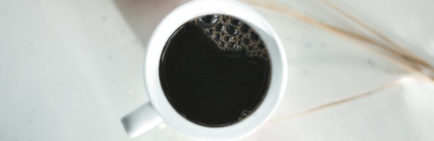 Cup of black coffee on a wooden surface next to a small notebook, illustrating the research-focused topic of coffee and diabetes
