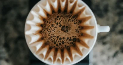 Top-down view of coffee blooming through a white fluted paper coffee filter set in a pour-over dripper, against a dark stone background