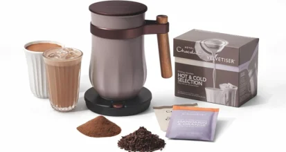 Electric hot chocolate maker beside a hot and an iced chocolate drink, a box of drinking chocolate sachets, cocoa powder and chocolate flakes