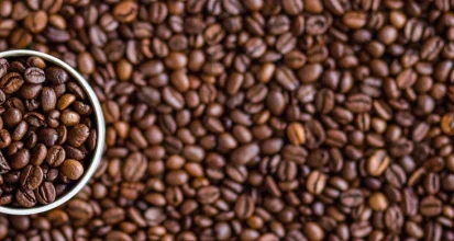 Overhead view of a white coffee cup filled with and surrounded by roasted coffee beans