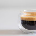 Double-walled glass cup of black coffee with a light layer of crema on a white table