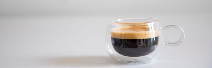 Double-walled glass cup of black coffee with a light layer of crema on a white table