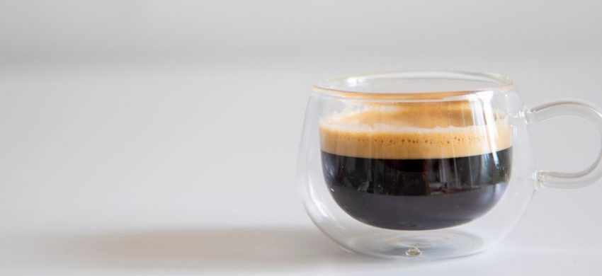 Double-walled glass cup of black coffee with a light layer of crema on a white table
