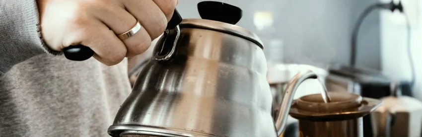An AeroPress, electric gooseneck kettle, hand grinder, and travel mug on a small wooden dorm desk