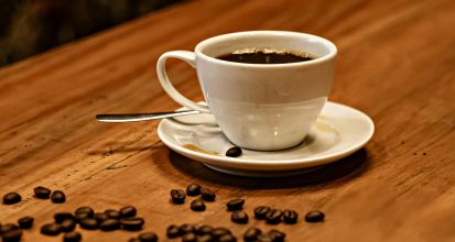 A cup of black coffee on a table beside scattered roasted coffee beans, illustrating premium specialty coffee