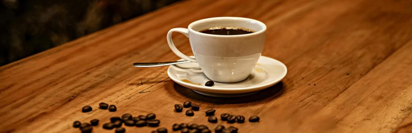 A cup of black coffee on a table beside scattered roasted coffee beans illustrating premium specialty coffee
