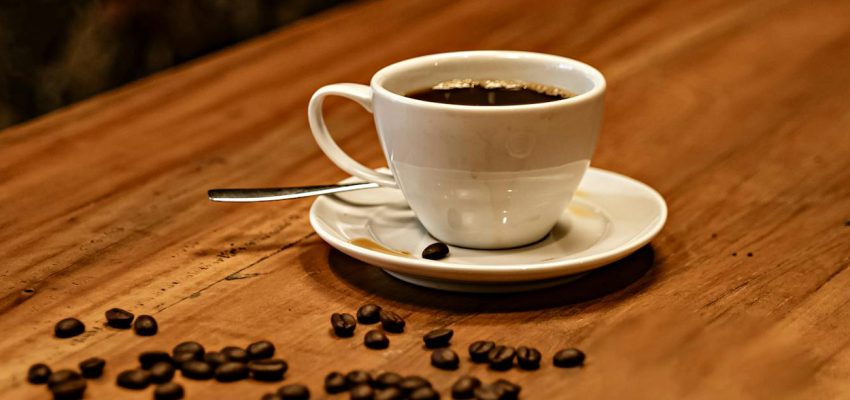 A cup of black coffee on a table beside scattered roasted coffee beans illustrating premium specialty coffee