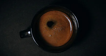 Overhead view of a single cup of black coffee with no milk or sugar on a dark surface