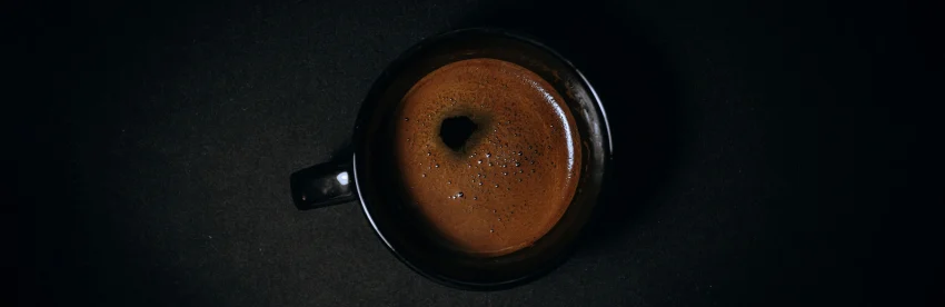 Overhead view of a single cup of black coffee with no milk or sugar on a dark surface