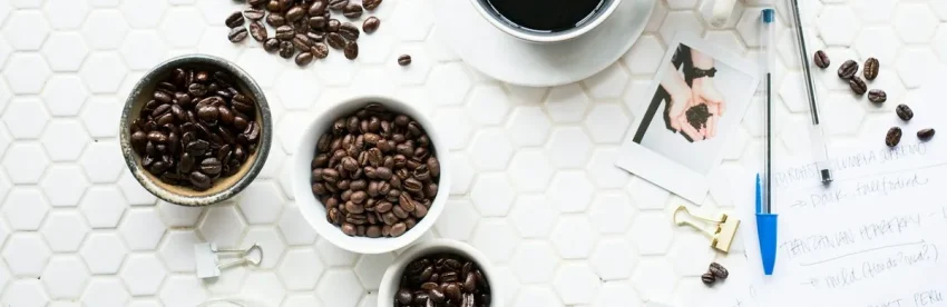 Bowls of different single-origin coffee beans beside handwritten tasting notes and a cup of black coffee