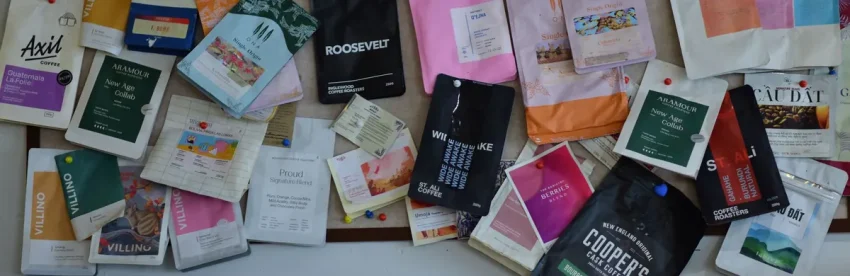 A colorful pinboard covered in coffee bags from many different roasters and brands, each with distinct packaging design
