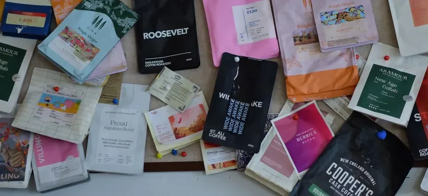 A colorful pinboard covered in coffee bags from many different roasters and brands, each with distinct packaging design