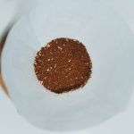 Overhead view of a bed of medium-ground coffee sitting in a white paper filter cone, showing the varied particle texture and lighter chaff