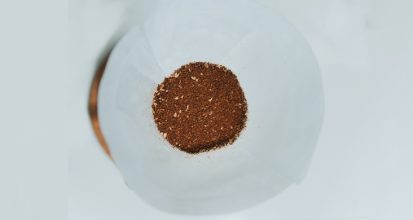 Overhead view of a bed of medium-ground coffee sitting in a white paper filter cone, showing the varied particle texture and lighter chaff