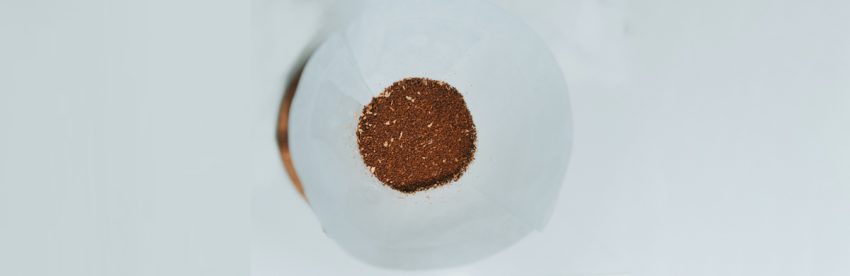 Overhead view of a bed of medium-ground coffee sitting in a white paper filter cone, showing the varied particle texture and lighter chaff