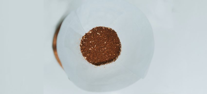 Overhead view of a bed of medium-ground coffee sitting in a white paper filter cone, showing the varied particle texture and lighter chaff