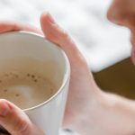 Woman warming her hands around a mug of coffee in soft morning light