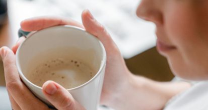 Woman warming her hands around a mug of coffee in soft morning light