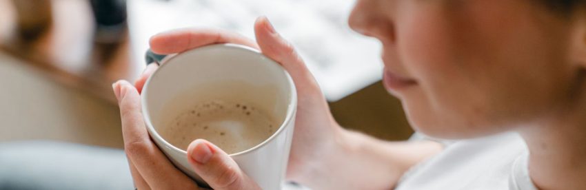 Woman warming her hands around a mug of coffee in soft morning light