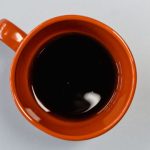 Overhead view of a burnt orange ceramic mug of black coffee gone cold and still, sitting on a plain pale grey surface