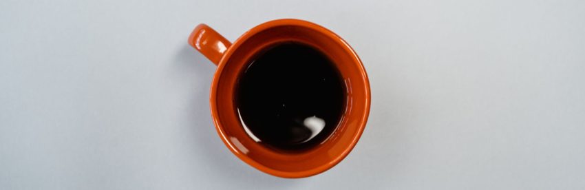Overhead view of a burnt orange ceramic mug of black coffee gone cold and still, sitting on a plain pale grey surface