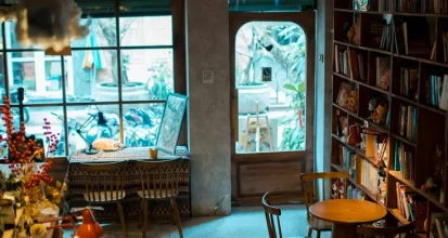 The warm, characterful interior of an independent coffee shop, with floor-to-ceiling bookshelves, mismatched furniture, and daylight streaming through a large window
