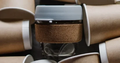 A single reusable coffee cup with a cork sleeve surrounded by dozens of discarded disposable paper coffee cups, illustrating the waste difference