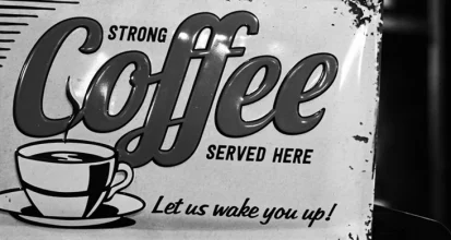 Weathered black and white enamel sign reading Strong Coffee Served Here, Let us wake you up, with a drawing of a steaming cup and saucer