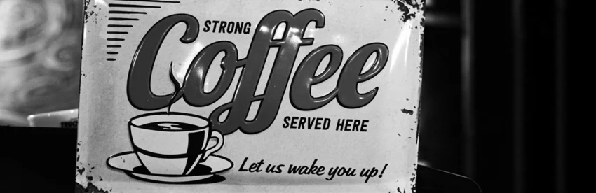 Weathered black and white enamel sign reading Strong Coffee Served Here, Let us wake you up, with a drawing of a steaming cup and saucer