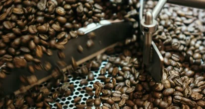 Roasted coffee beans in motion inside a stainless steel roaster cooling tray, stirred by a rotating metal arm