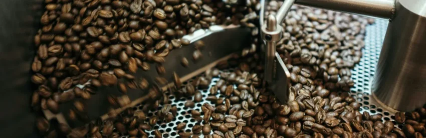 Roasted coffee beans in motion inside a stainless steel roaster cooling tray, stirred by a rotating metal arm