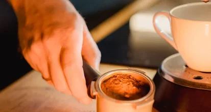 A hand seating a portafilter of freshly dosed ground coffee into an espresso machine