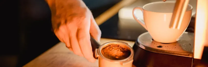 A hand seating a portafilter of freshly dosed ground coffee into an espresso machine