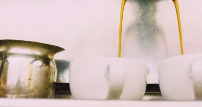 Espresso streaming from the group head of a vintage-style brass espresso machine into two white cups, with a milk pitcher beside them